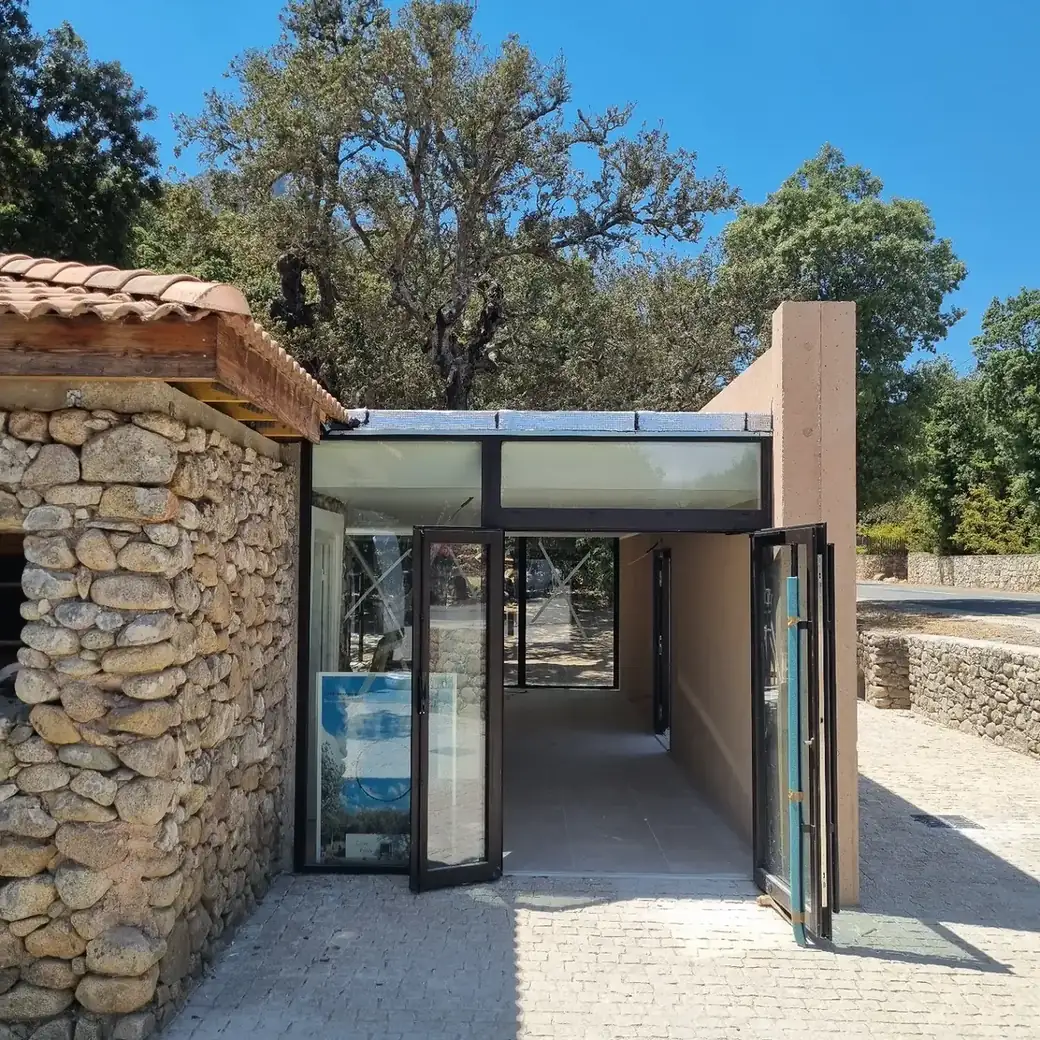 Pavillon vitré accolé à un bâtiment en pierre, mur d’enduit ocre au premier plan
